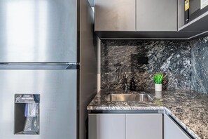 A kitchen with a stainless steel refrigerator, a granite countertop, a sink, and a small potted plant. - Soho Village en Palermo by Magno | 901 (Buenos Aires)