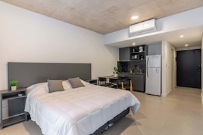 A modern hotel room with a bed, bedside tables, a desk, a kitchenette, and an air conditioning unit. - Soho Village en Palermo by Magno | 102 (Buenos Aires)