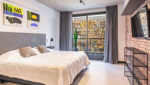 Ein modernes Schlafzimmer mit einem großen Bett, einem Balkon mit Blick und abstrakter Wandkunst.