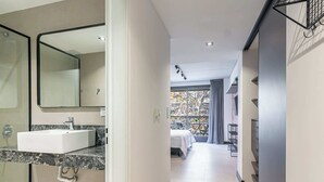 Ein modernes Hotelzimmer mit Marmor-Waschtisch, einem großen Spiegel, einem Bett mit weißer Bettdecke, einem Balkon mit Blick und einer kleinen Sitzecke.