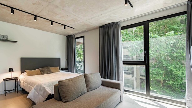 Ein modernes Schlafzimmer mit Bett, Sofa und großen Fenstern.