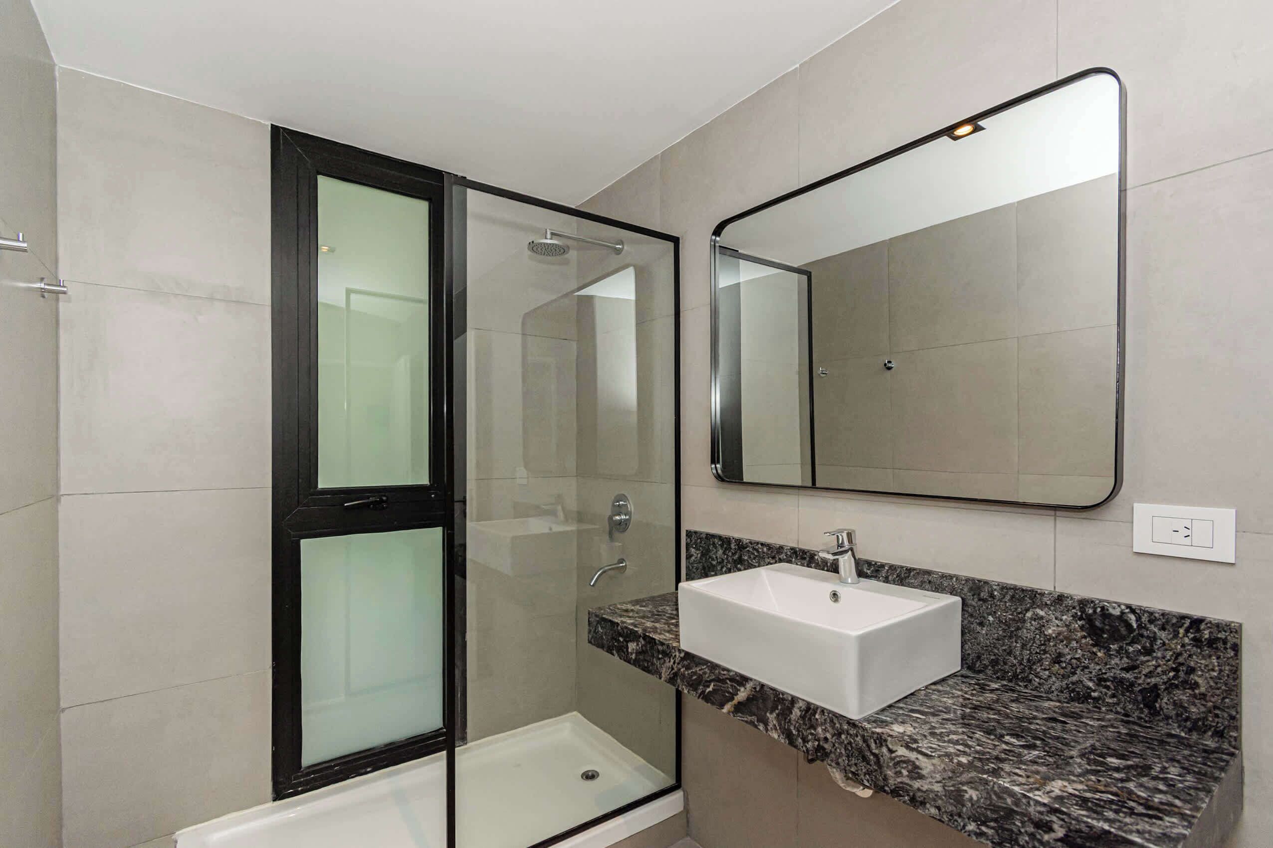 Un baño moderno con ducha envuelta en vidrio, un lavamanos blanco con encimera de mármol y un espejo grande.