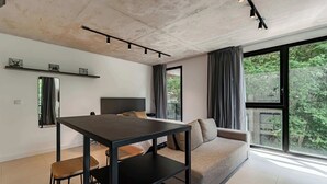 Ein modernes Wohnzimmer mit einer Couch, einem Esstisch und einem großen Fenster mit Blick auf Grünflächen.