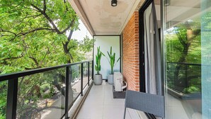 Ein Balkon mit Glasgeländer, Blumentöpfen, einem Tisch und einem Stuhl.