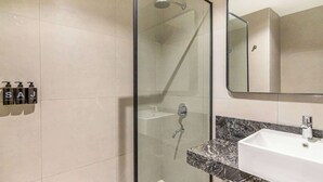Een moderne badkamer met een douchecabine van glas, een witte wastafel en een spiegel erboven.