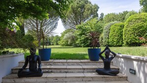 A garden with steps leading up to a seating area with two statues.