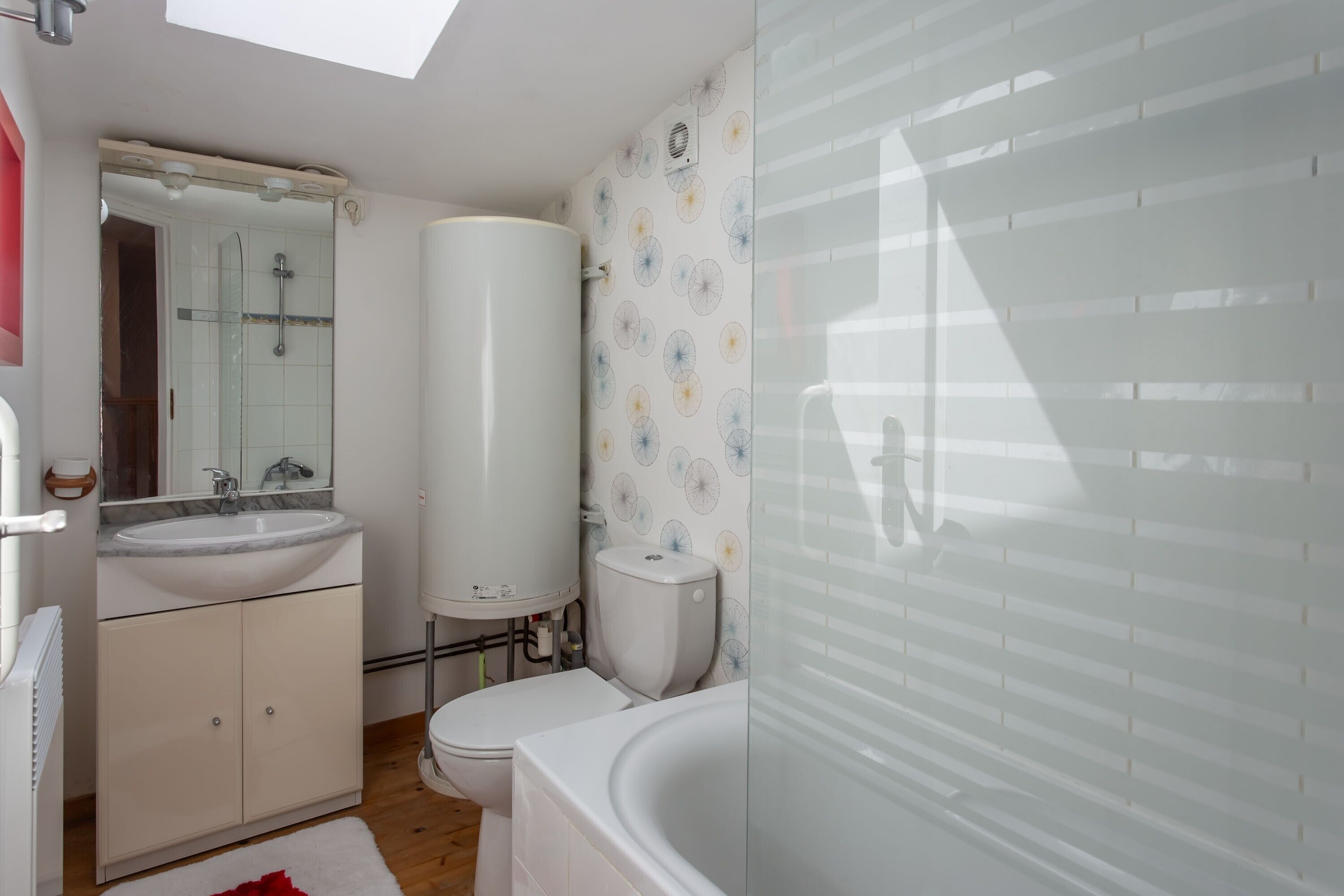 Un bagno moderno con un lucernario, una vasca da bagno bianca capiente, un water e un lavandino.
