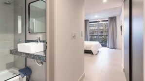 Un baño moderno con ducha de vidrio, lavabo blanco y un espejo grande.