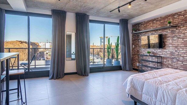 Een moderne slaapkamer met een groot raam, een bed, een televisie en een klein tafeltje met stoelen.