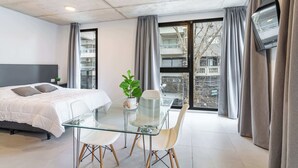 A modern hotel room with a bed, a glass dining table, chairs, a potted plant, and a TV mounted on the wall. - Soho Village en Palermo by Magno | 203 (Buenos Aires)