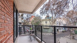 A balcony with a table and chairs, a brick wall, and a view of a street with buildings and trees. - Soho Village en Palermo by Magno | 203 (Buenos Aires)