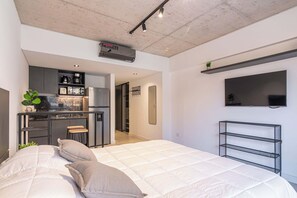 A modern bedroom with a bed, a small kitchenette, and a TV mounted on the wall. - Soho Village en Palermo by Magno | 602 (Buenos Aires)