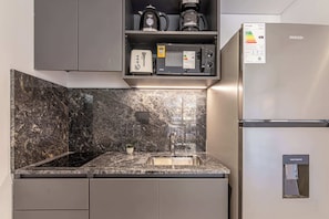 A kitchen with a built-in microwave, toaster, and coffee maker on a shelf, a water dispenser on the refrigerator, and a granite countertop. - Soho Village en Palermo by Magno | 602 (Buenos Aires)