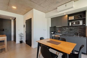 A modern kitchen with a dining area, including a wooden table and chairs, a microwave, and a stove. - Soho Village en Palermo by Magno | 504 (Buenos Aires)