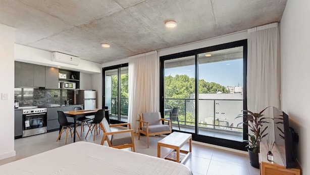 Ein modernes Hotelzimmer mit einem großen Bett, einer Essecke, einer Küchenzeile und einem Balkon mit Blick.