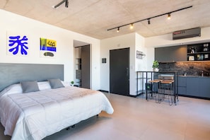A modern bedroom with a bed, a small kitchenette, and a door leading to another room. - Soho Village en Palermo by Magno | 604 (Buenos Aires)