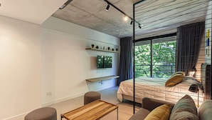 Ein modernes Schlafzimmer mit Bett, Fernseher, kleinem Tisch und einem Fenster mit Vorhängen.