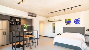 Una camera d'albergo moderna con angolo cottura, un letto, un tavolino con sgabelli e uno specchio.