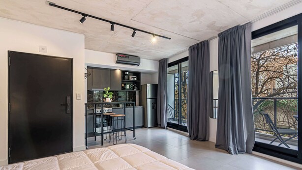 Un dormitorio moderno con una cama grande, una kitchenette y un cerramiento de vidrio corredizo al exterior.
