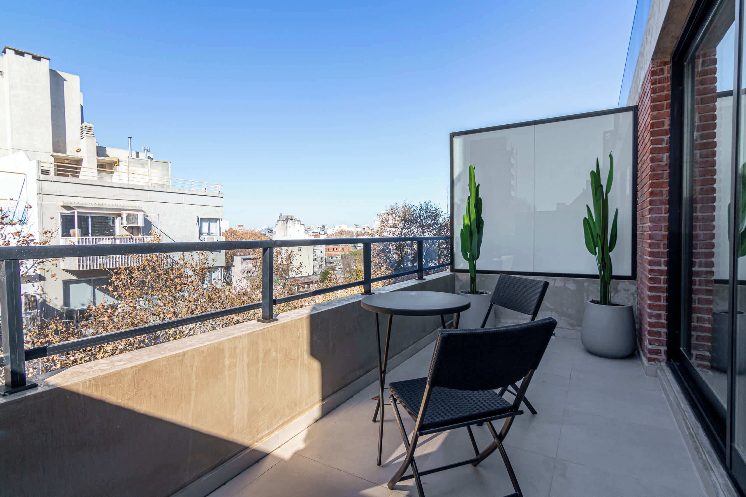 Ein Balkon mit Tisch und Stühlen, Blumentöpfen und Blick auf Gebäude.