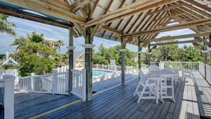 En överbyggd träveranda med vita räcken, en pool och utemöbler.