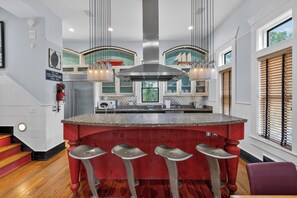 A kitchen with a central island, bar stools, a stainless steel range hood, pendant lights, and a view of the outdoors through windows. - Emil Cottage- Luxary 4-bedroom in Coast Cottages  was featured on HGTV (St. Simons Island)