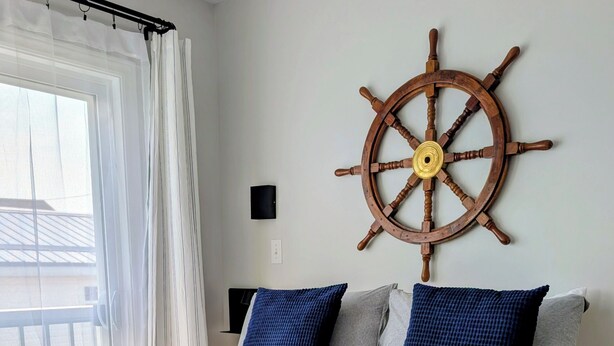 A bed with a blue and white bedspread, two pillows, a rolled white towel, and a wooden ship's wheel on the wall. - Lockeport Inn (Lockeport)