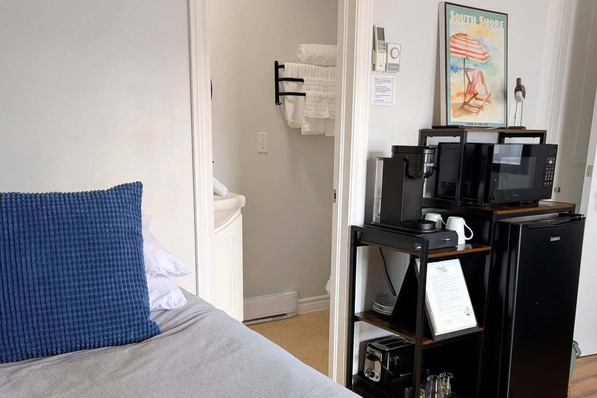 Et hotelværelse med en seng, et lille tekøkken, en mikrobølgeovn, en brødrister og et billede i ramme på væggen.