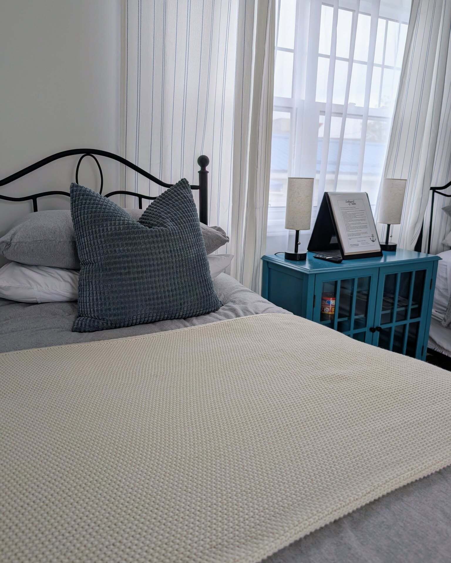 A bed with a textured blanket, pillows, a nightstand with lamps, and a sign.