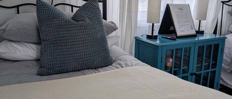A bed with a textured blanket, pillows, a nightstand with lamps, and a sign.