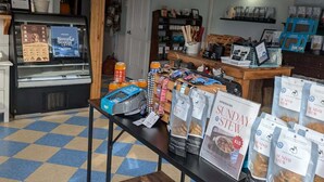 A café interior with a checkered floor, wooden ceiling beams, and a display table with bags of Sunday Stew. - Lockeport Inn (Lockeport)