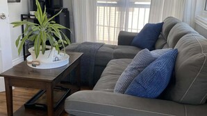 A living room with a grey sofa, a small table with a plant, and a TV mounted on the wall. - Lockeport Inn (Lockeport)