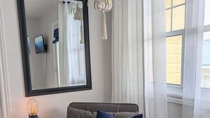 A modern living room with a grey sofa, a small side table with a lamp, a large mirror, and a hanging macrame plant. - Lockeport Inn (Lockeport)