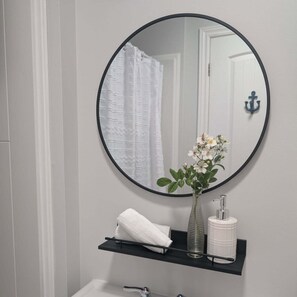A bathroom with a round mirror, a white towel, a glass vase with flowers, and a white toilet paper holder.