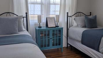 Un dormitorio con dos camas, una mesita con lámpara y una ventana con cortinas.