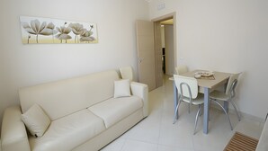 A modern living room with a sofa, a dining table with chairs, and a wall-mounted artwork. - Case Vacanza Edera - Orchidea near Trapani Port (Trapani)