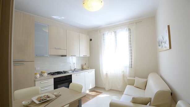 A modern kitchen with white cabinets, a dining table, and a sofa in a living area. - Case Vacanza Edera - Orchidea near Trapani Port (Trapani)