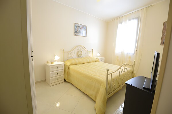 Une chambre à coucher avec un lit, des tables de chevet, une lampe, un téléviseur et une fenêtre avec des rideaux.