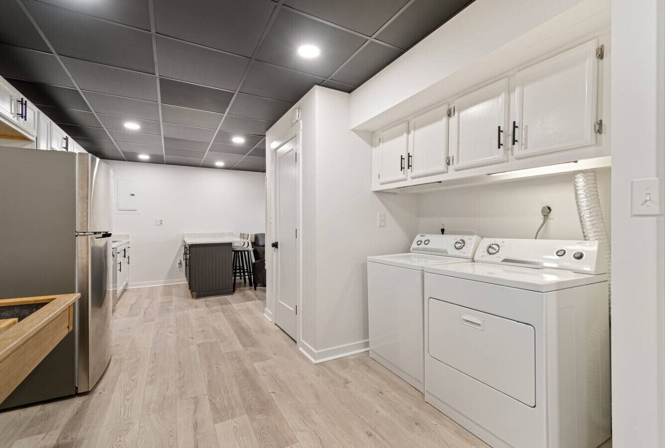 A modern kitchen with white cabinets, a stainless steel refrigerator, and a built-in washer and dryer.