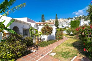 A white building with a tiled roof, a paved pathway, and lush greenery. - Tropicana 6C by Casasol (Nerja)