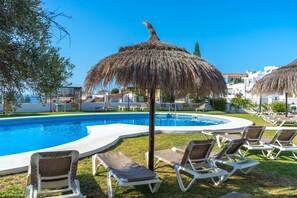 A swimming pool with lounge chairs and a thatched umbrella, surrounded by a white building with a curved pool edge. - Tropicana 6C by Casasol (Nerja)