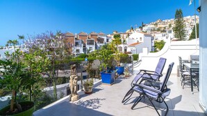 Une terrasse sur le toit, aménagée avec du mobilier d’extérieur, des plantes en pot et offrant une vue sur une ville située sur une colline.