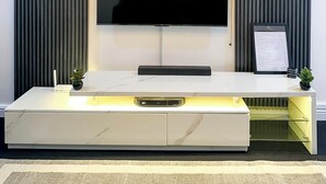 Ein modernes Wohnzimmer mit einem Wand-Fernseher, einer integrierten Unterhaltungseinheit darunter und einer Deckenleuchte.