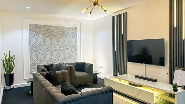Ein modernes Wohnzimmer mit einem Ecksofa, einem Flachbildfernseher, einer Wandverkleidung und einer Deckenleuchte.