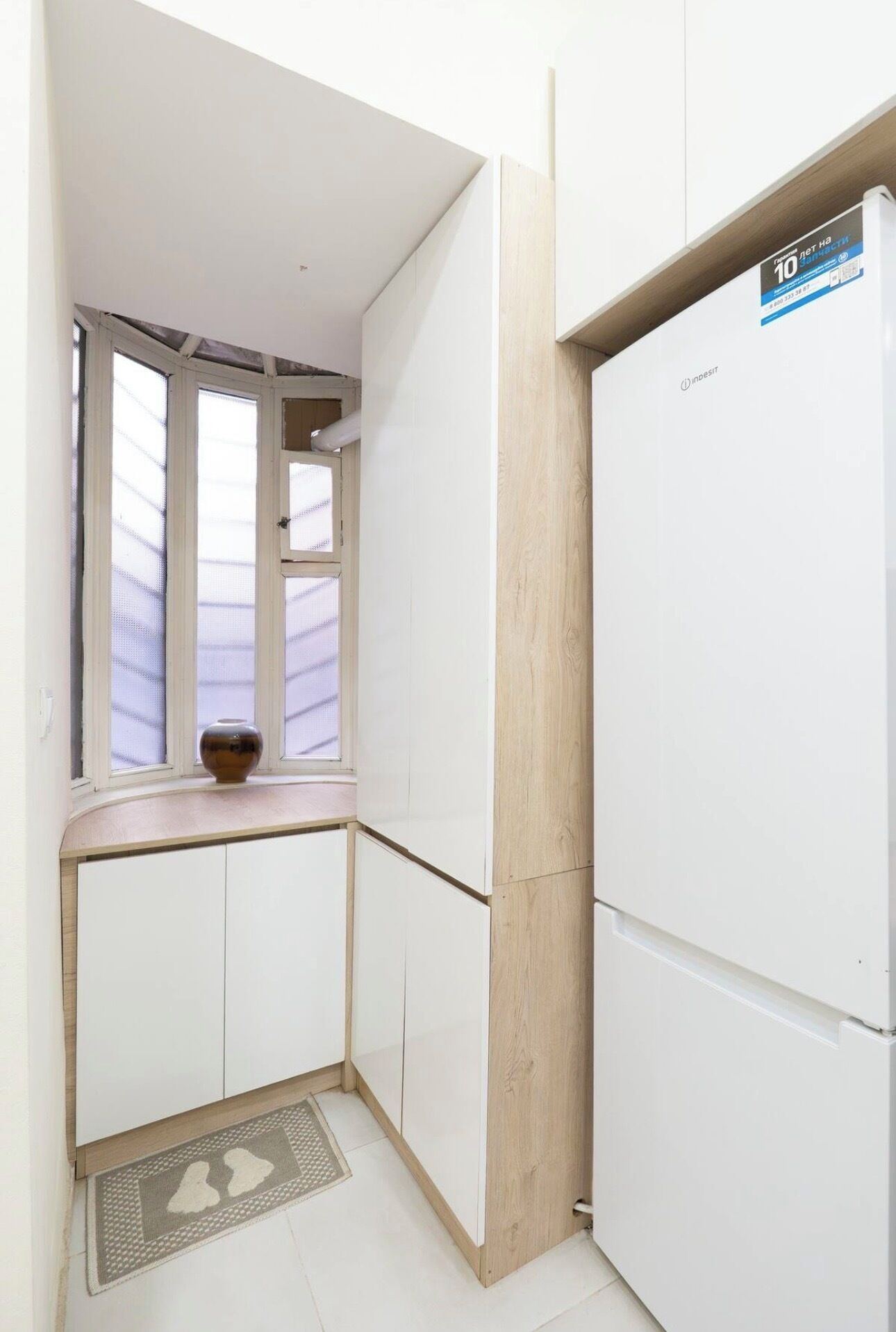 Una cocina pequeña con armarios blancos, un ventanal con vistas y un refrigerador.