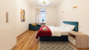 Un dormitorio con cama, mesita de noche, una silla, una ventana y un cuadro en la pared.
