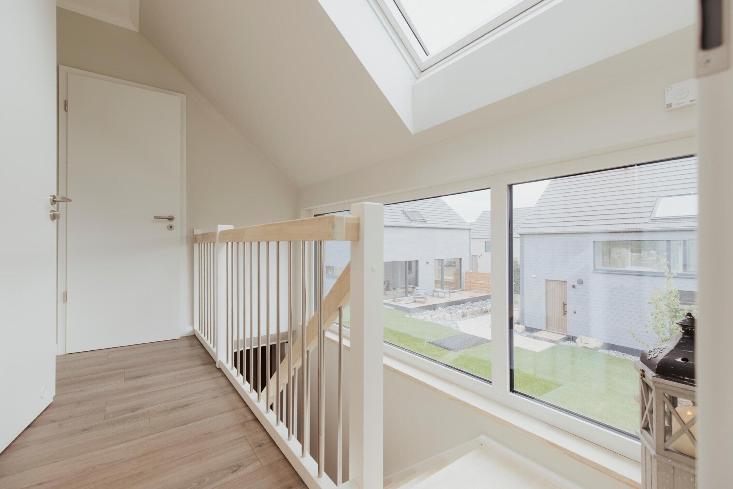 Een modern interieur met een houten trap, dakraam en uitzicht op een woonwijk.
