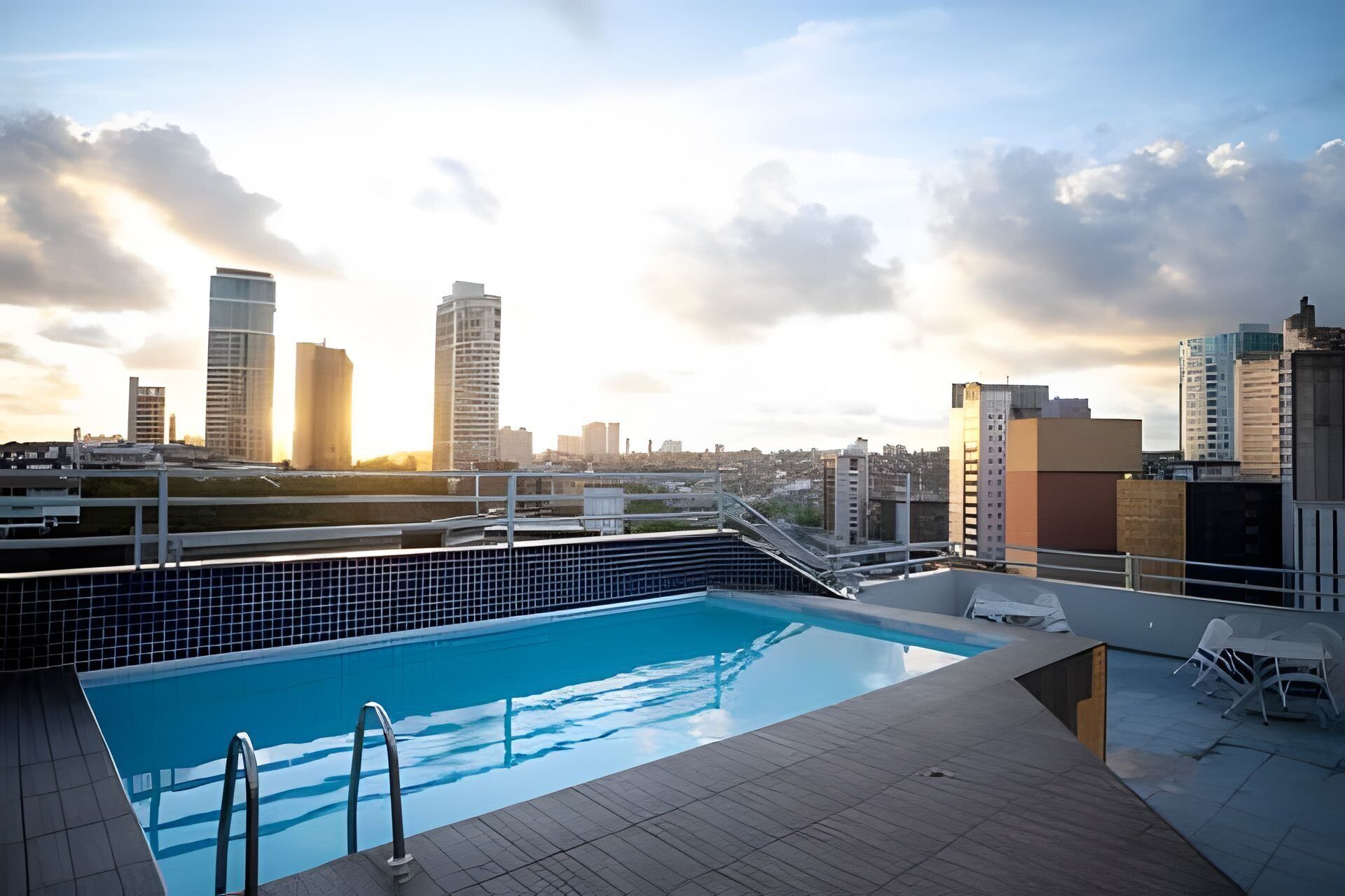 A rooftop pool with a cityscape view, including high-rise buildings and a clear sky.