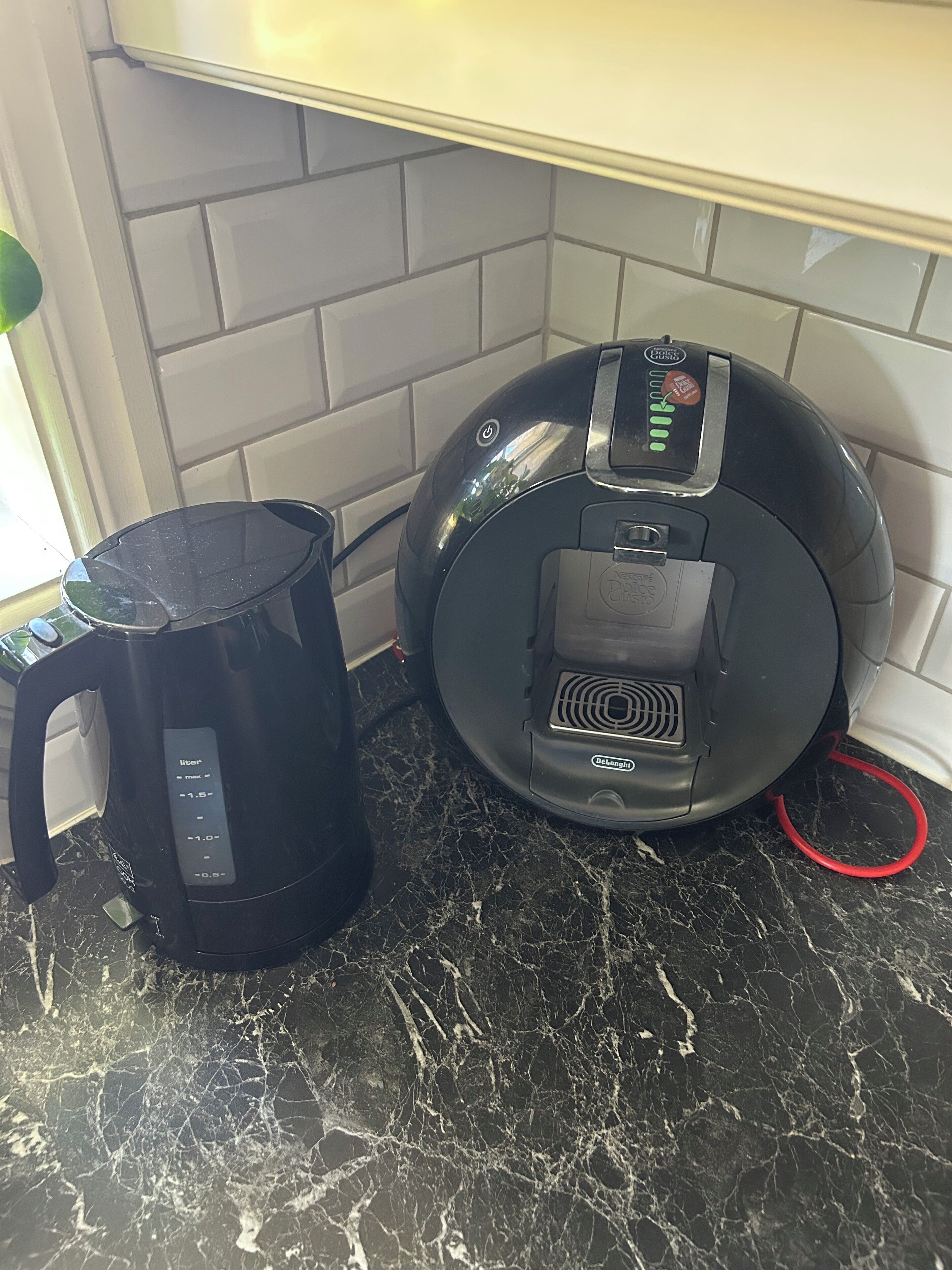 A black coffee maker and a black electric kettle on a marble countertop.
