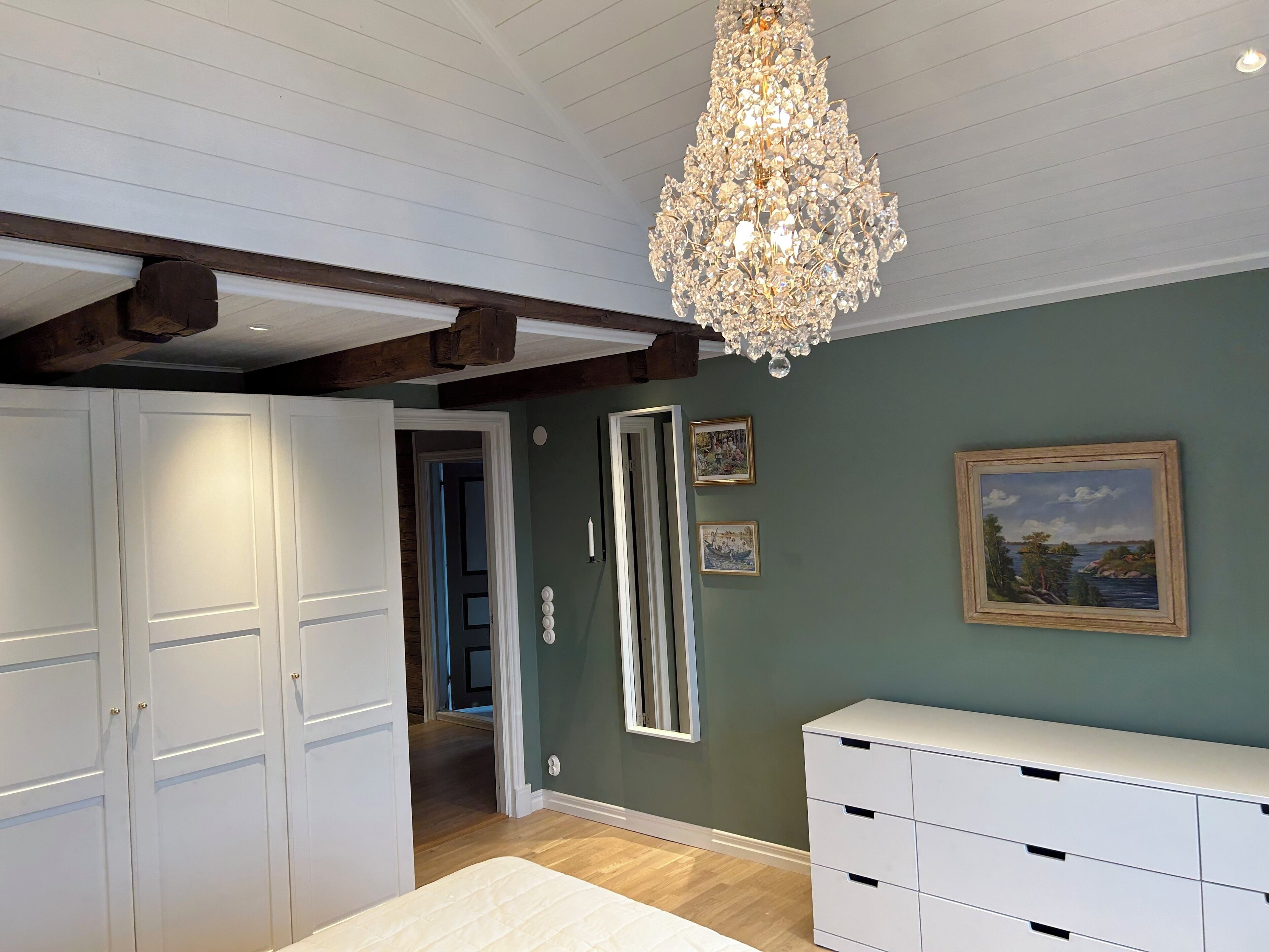 Een kamer met een kroonluchter, een witte garderobe, een spiegel en een schilderij aan de muur.